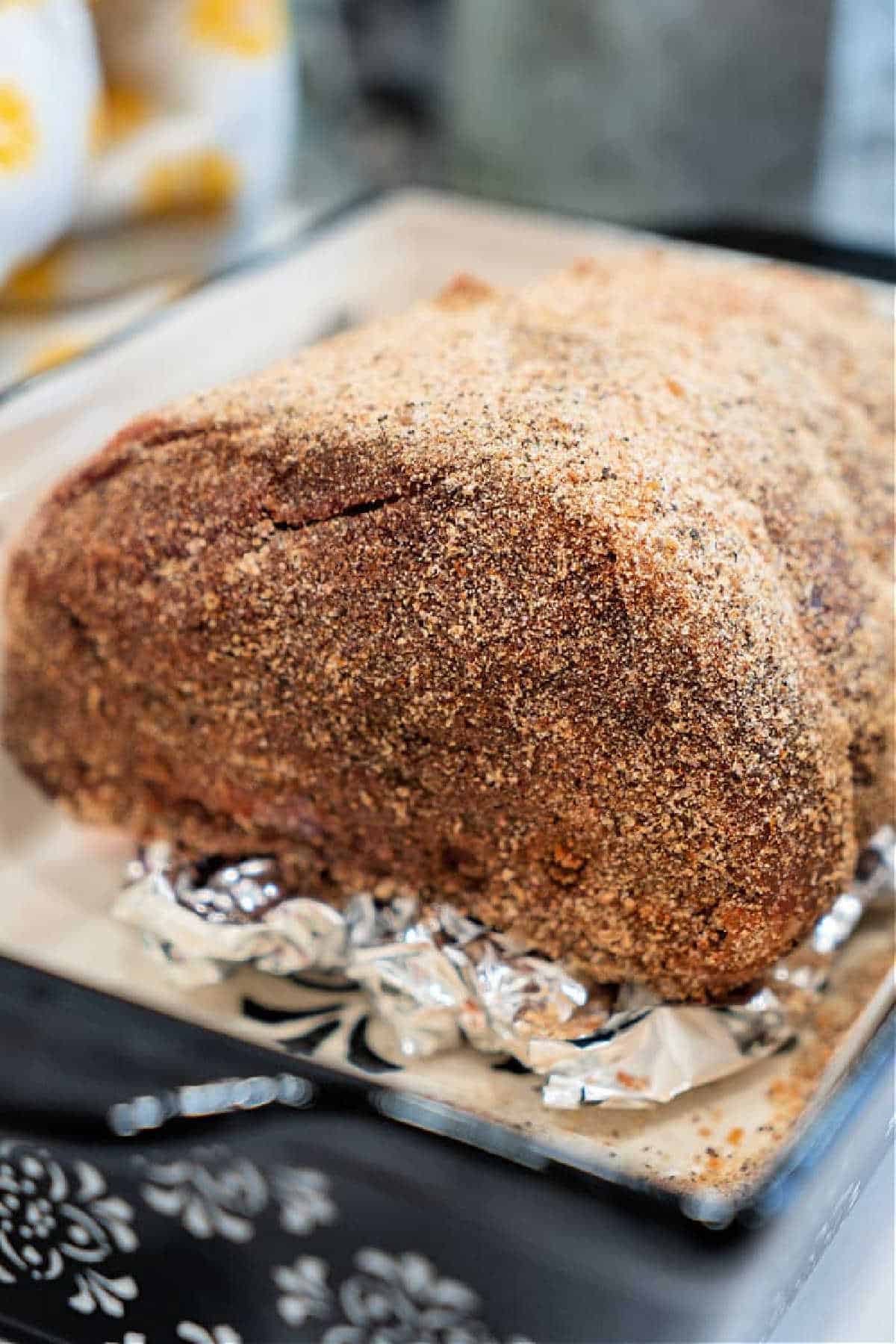 A large, seasoned top round roast recipe is covered in breadcrumbs and sits in a pan lined with foil, ready to be cooked.