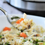 A spoonful of Instant Pot chicken rice soup is held above a white bowl, with an appliance in the background.