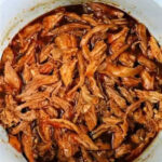 Shredded barbecue chicken in a white slow cooker with rich, brown sauce, perfect for those who also love making pork butt in the Instant Pot.