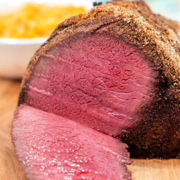 Sliced Top Round Roast Recipe with a peppered crust on a wooden cutting board, showing a juicy pink interior.
