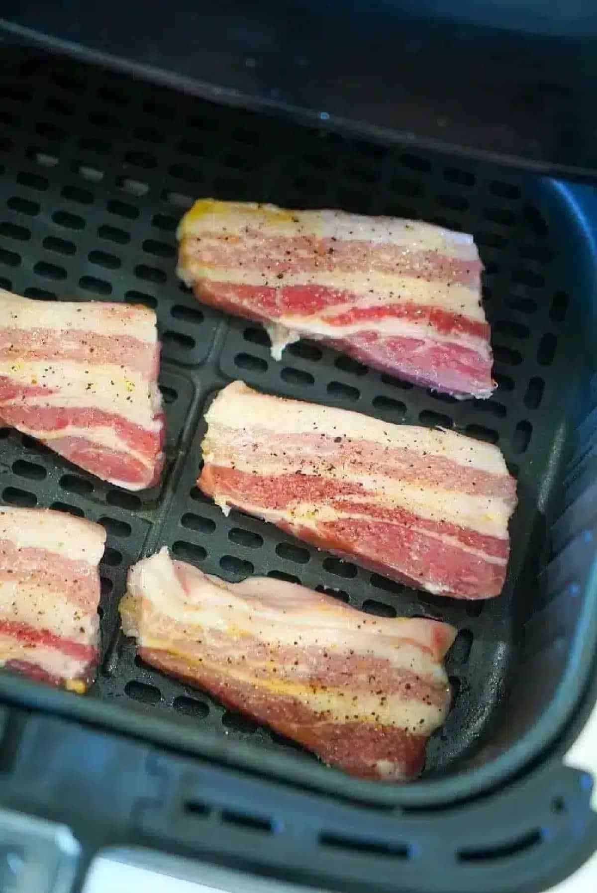 Raw, seasoned air fryer pork belly strips arranged inside the basket, ready to be cooked.