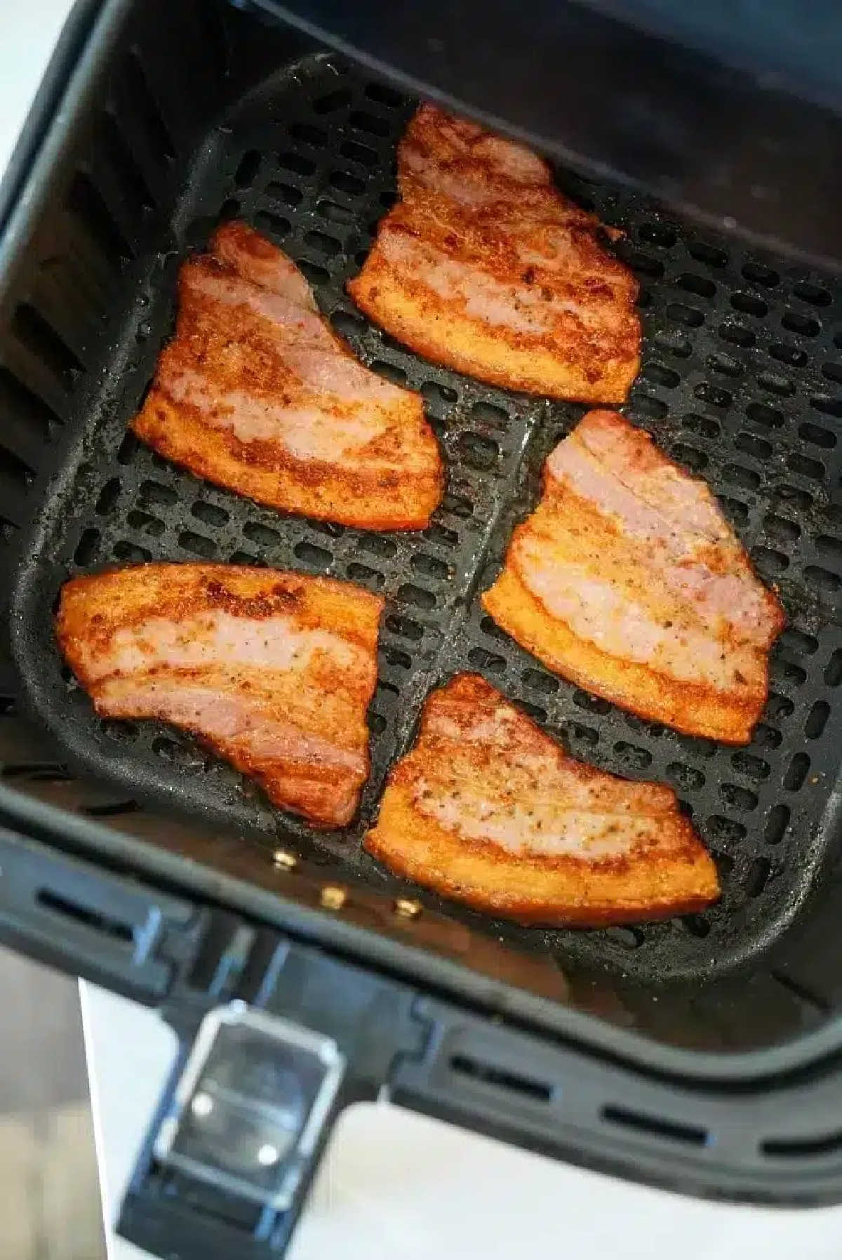 Five pieces of seasoned air fryer pork belly sizzle in the basket, crisping up to perfection.