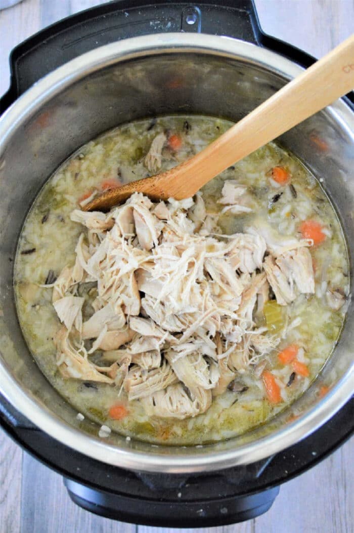 Shredded chicken, vegetables, and rice simmer together in this flavorful instant pot chicken rice soup, all stirred gently with a wooden spoon.