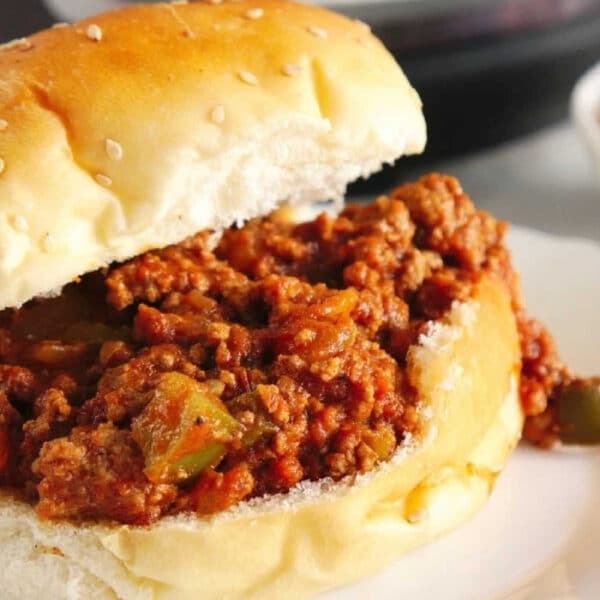 Instant Pot Sloppy Joes sandwich with saucy ground beef filling on a sesame bun, served on a white plate.