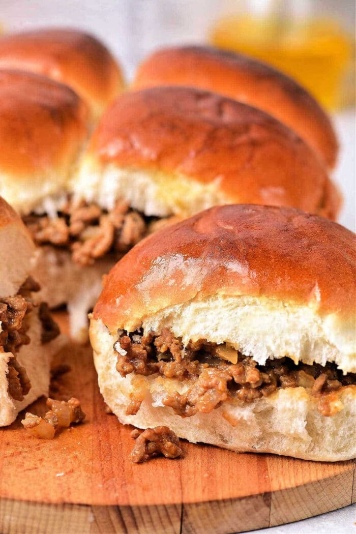 Four instant pot sloppy joe sliders filled with ground beef and onions on a wooden serving board.