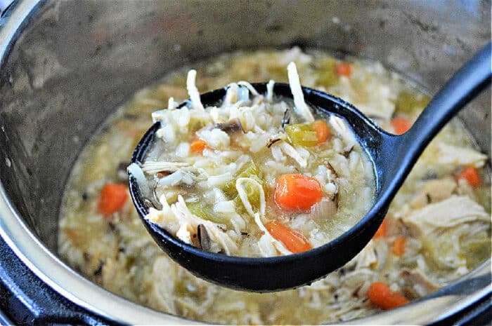 A ladle of Instant Pot chicken rice soup with carrots and celery held over a pot.