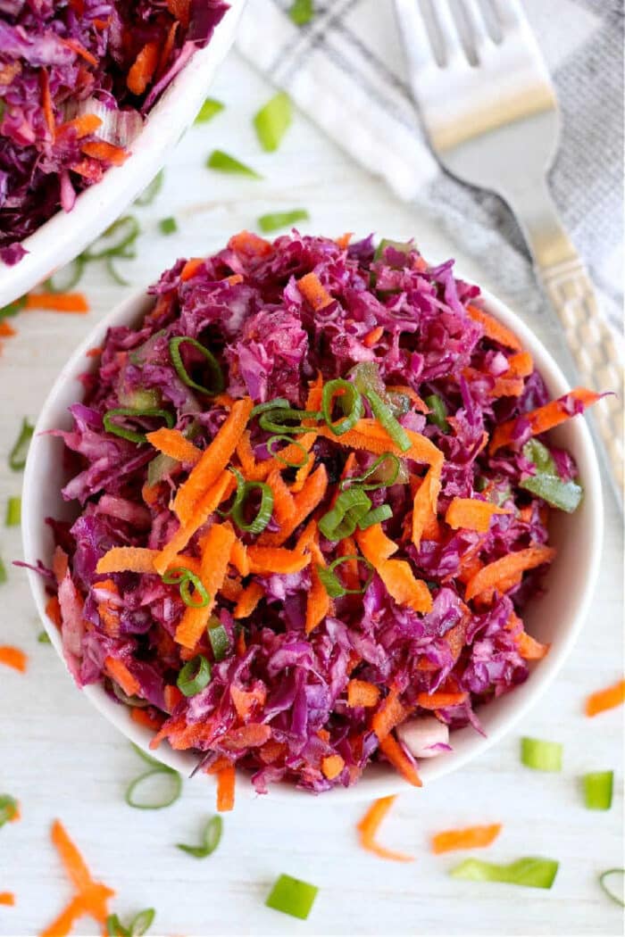 A bowl of colorful red cabbage coleslaw with shredded carrots and chopped green onions.