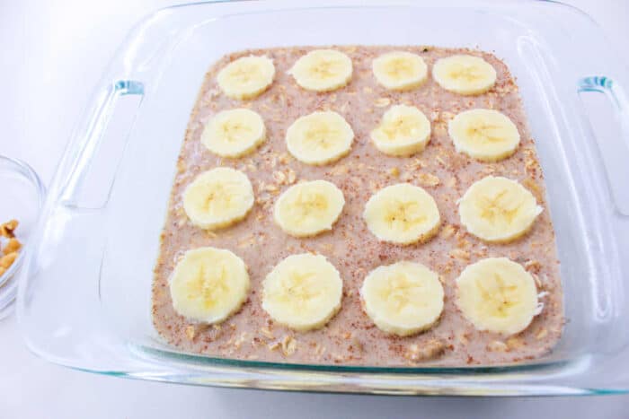 A glass baking dish with Banana Oatmeal batter, topped with banana slices, ready to be baked.