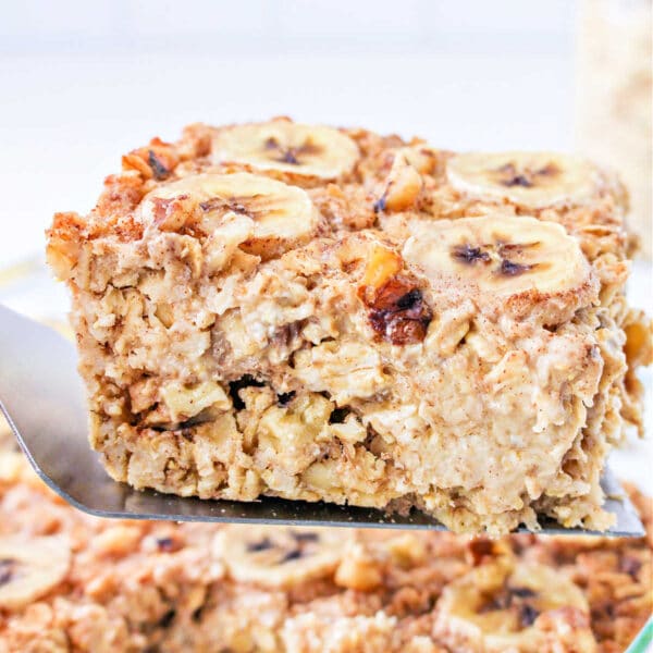 A spatula lifts a square of Banana baked Oatmeal, topped with fresh banana slices and crunchy nuts.