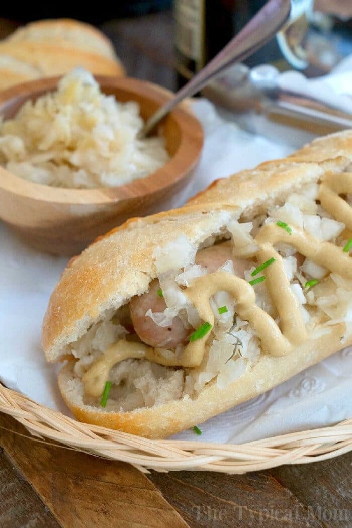 Instant Pot brats and sauerkraut taste amazing! Easy way to steam bratwurst or sausage with some beer in your pressure cooker for dinner. #instantpot #pressurecooker #brats #bratwurst #sausage #instantpotrecipes #ninjafoodi An instant pot brats sausage in a bun topped with sauerkraut, mustard, and chives, served in a basket with extra sauerkraut in a bowl.