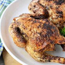 Two roasted, seasoned Cornish hens on a white plate with a plaid cloth in the background, perfect for learning how long to cook Cornish hen in air fryer for tender, flavorful results.