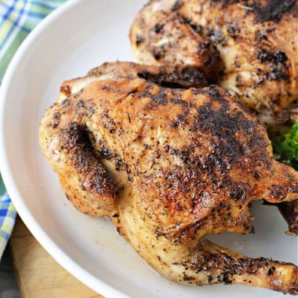 Two roasted, seasoned Cornish hens on a white plate with a plaid cloth in the background, perfect for learning how long to cook Cornish hen in air fryer for tender, flavorful results.