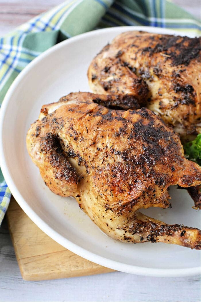 Two roasted, seasoned Cornish hens on a white plate with a plaid cloth in the background, perfect for learning how long to cook Cornish hen in air fryer for tender, flavorful results.
