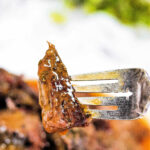 A close-up of a fork holding a juicy, glazed piece of arm roast with herbs—a delicious result from a slow cooker.