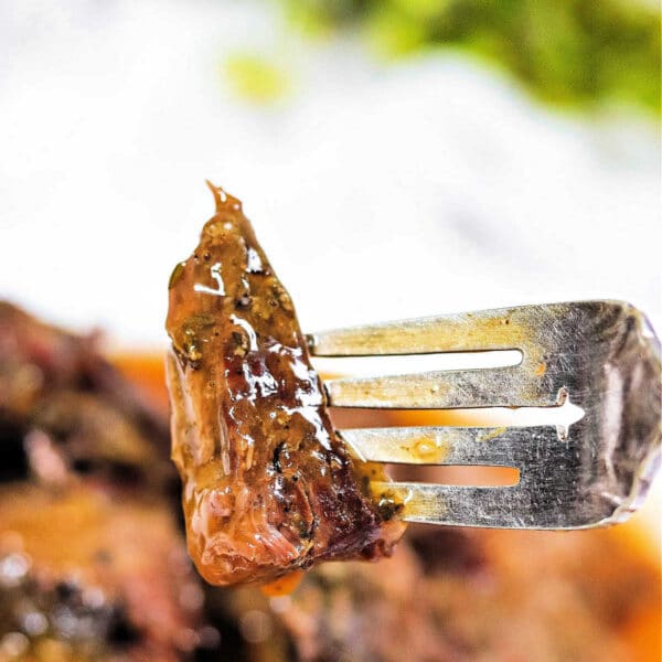 A close-up of a fork holding a juicy, glazed piece of arm roast with herbs—a delicious result from a slow cooker.