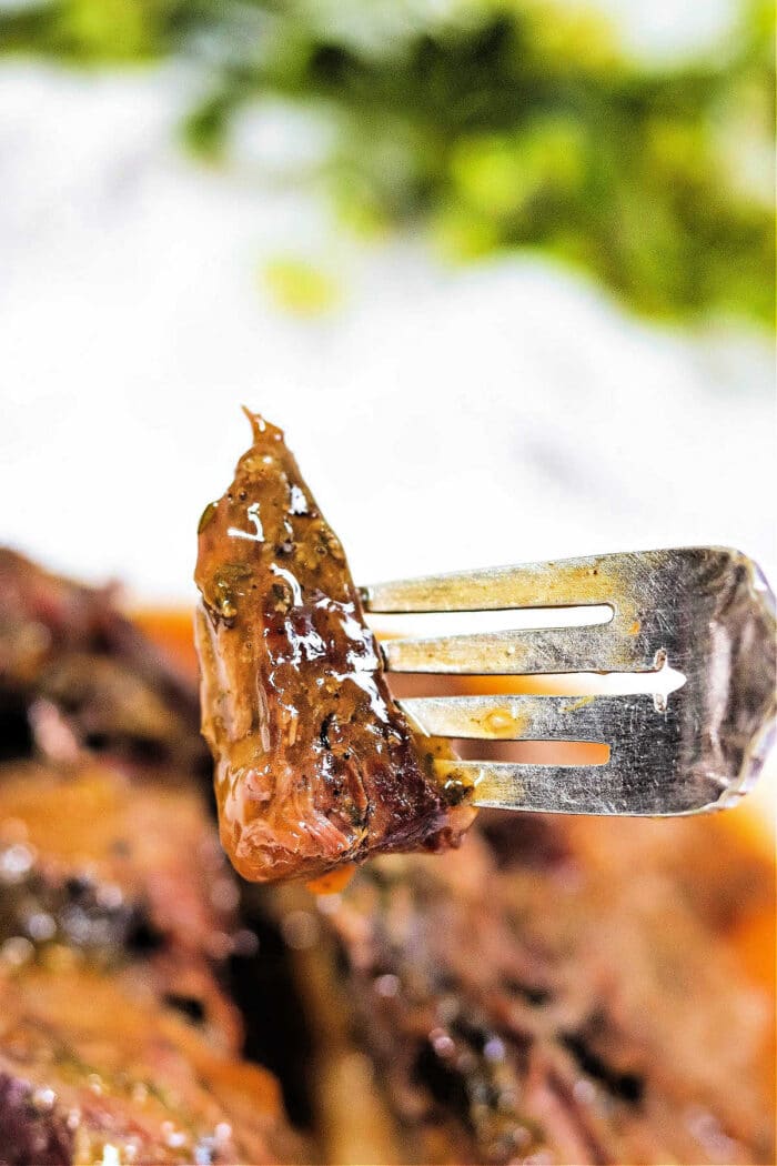 A close-up of a fork holding a juicy, glazed piece of arm roast with herbs—a delicious result from a slow cooker.