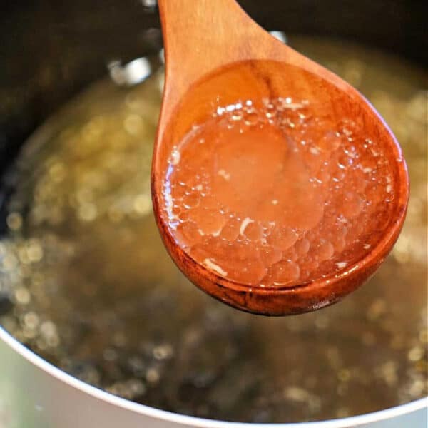 A wooden spoon holds hot gelatinous broth over a pot, showcasing the rich results of a Bone Broth Recipe made in an Instant Pot.