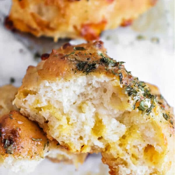 Close-up of a cheesy biscuit inspired by Bisquick Cheddar Bay Biscuits, topped with herbs and partially broken open to reveal its soft, airy inside.