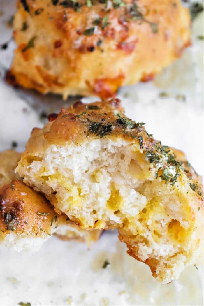 Close-up of a cheesy biscuit inspired by Bisquick Cheddar Bay Biscuits, topped with herbs and partially broken open to reveal its soft, airy inside.