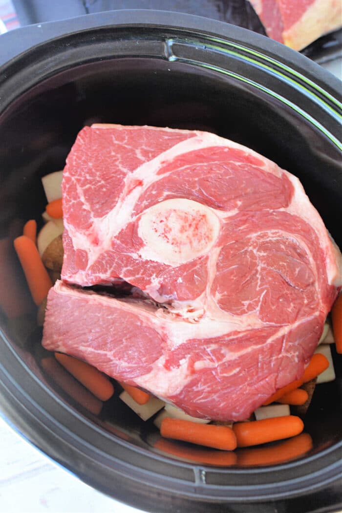 Arm Roast nestled atop carrots and potatoes inside a black Slow Cooker, making this Arm Roast Recipe both hearty and convenient.