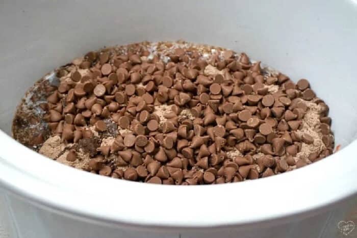 Chocolate chips on top of a layer of dry ingredients in a white crockpot, ready to become a rich and gooey crockpot lava cake with cake mix.