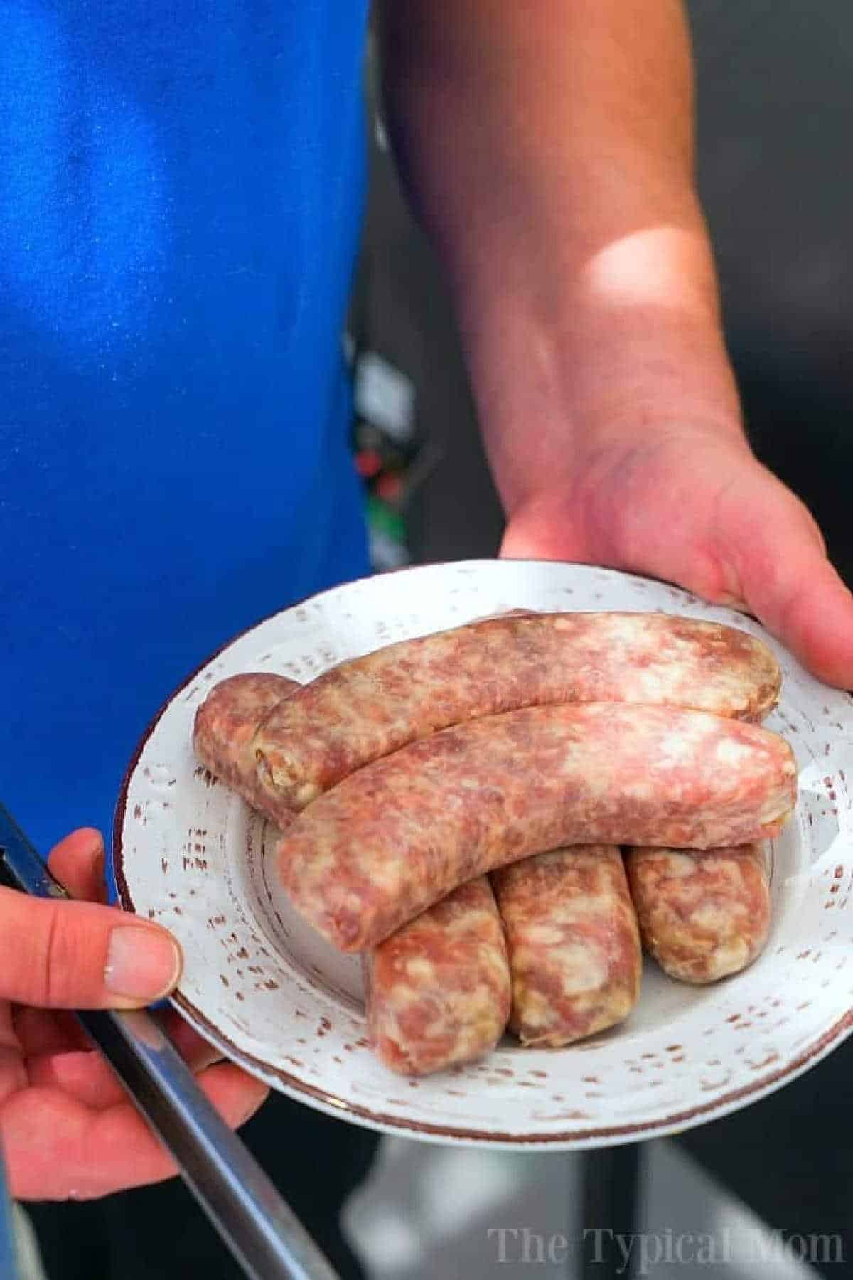Person holding a plate of raw sausages, wearing a blue shirt, ready to cook some instant pot brats.