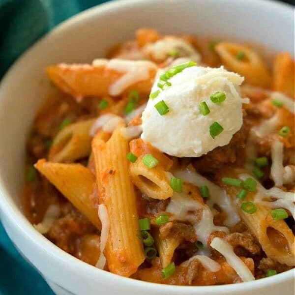 Bowl of penne pasta with tomato sauce, ground meat, melted cheese, chives, and a dollop of ricotta cheese—like a deconstructed pressure cooker lasagna casserole for effortless comfort food.