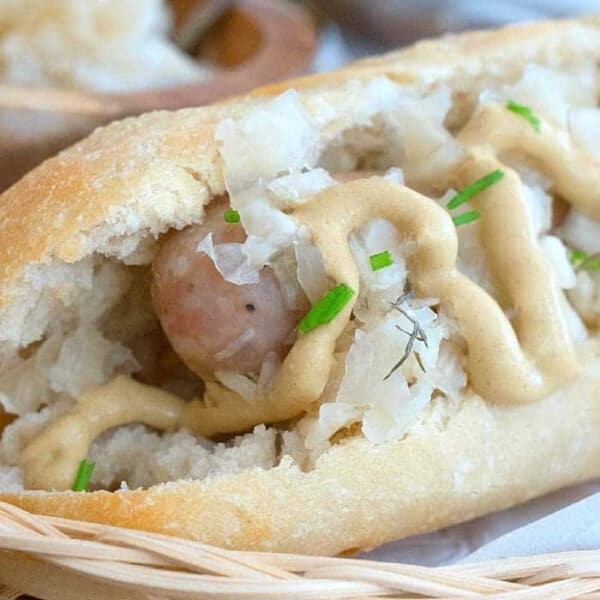 An instant pot brats sausage in a bun topped with sauerkraut, mustard, and chopped chives in a basket.