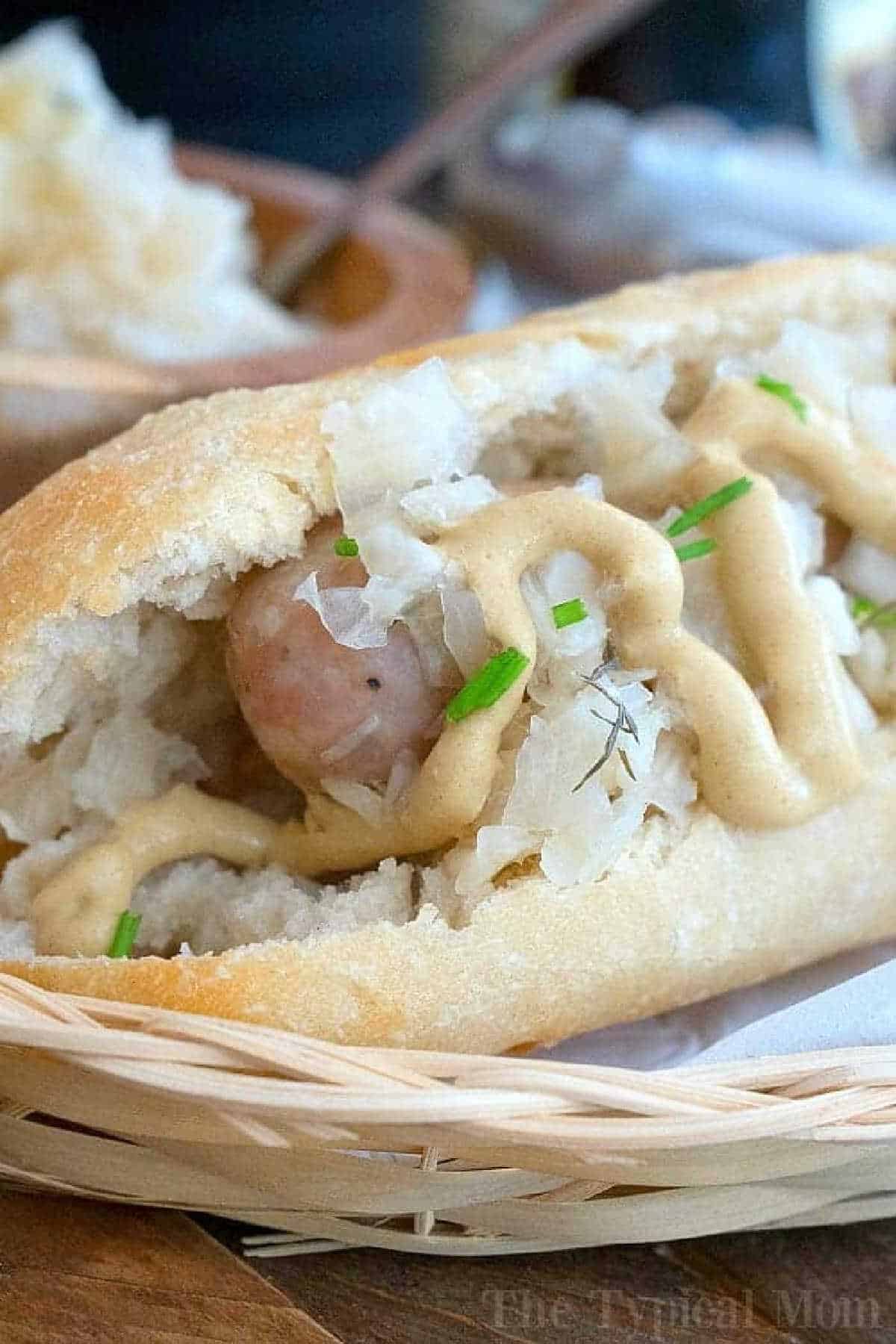 Instant Pot brats and sauerkraut taste amazing! Easy way to steam bratwurst or sausage with some beer in your pressure cooker for dinner. #instantpot #pressurecooker #brats #bratwurst #sausage #instantpotrecipes #ninjafoodi An instant pot brats sausage in a bun topped with sauerkraut, mustard, and chopped chives in a basket.