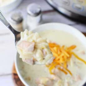 A spoonful of creamy Chicken Crack Soup above a bowl, with shredded cheese and an Instant Pot in the background.