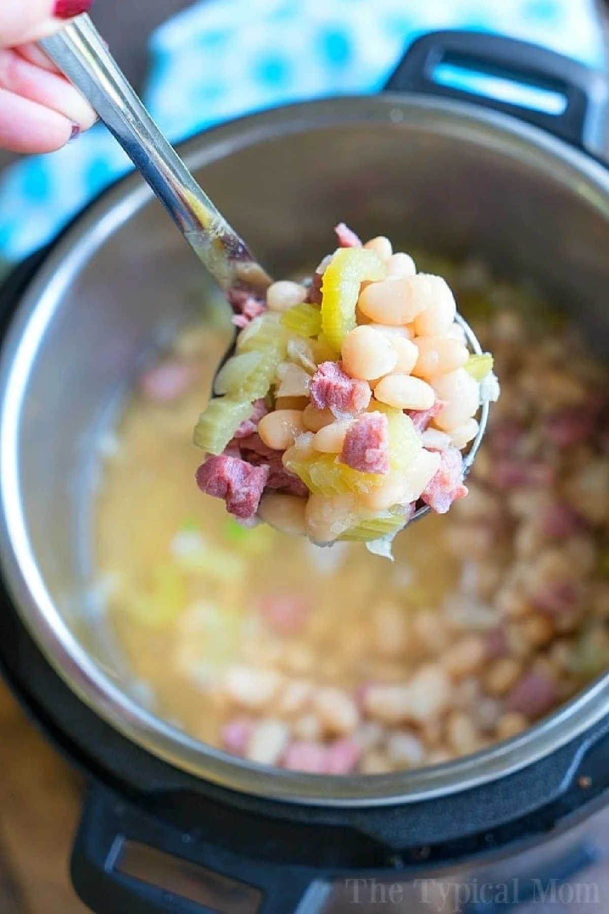 A spoonful of ham and white bean soup held over an Instant Pot filled with hearty pressure cooker ham and beans.
