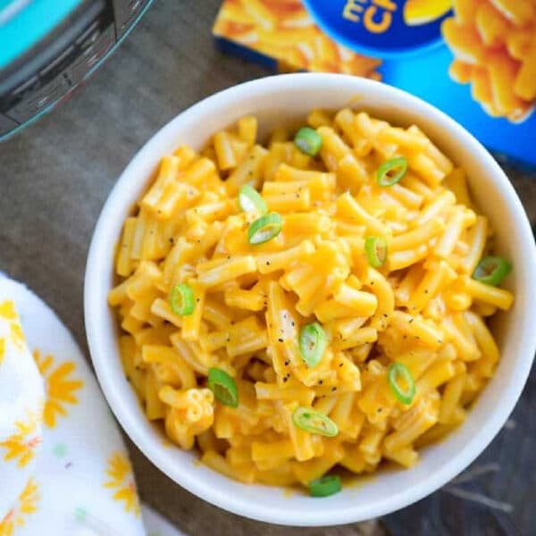 Bowl of macaroni and cheese topped with green onions next to a box of Kraft mac and cheese, perfect for making kraft mac and cheese in a pressure cooker.