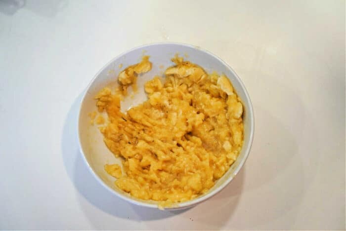 White bowl filled with mashed bananas, perfect for topping your Bananas and Cream Oatmeal, on a white surface.