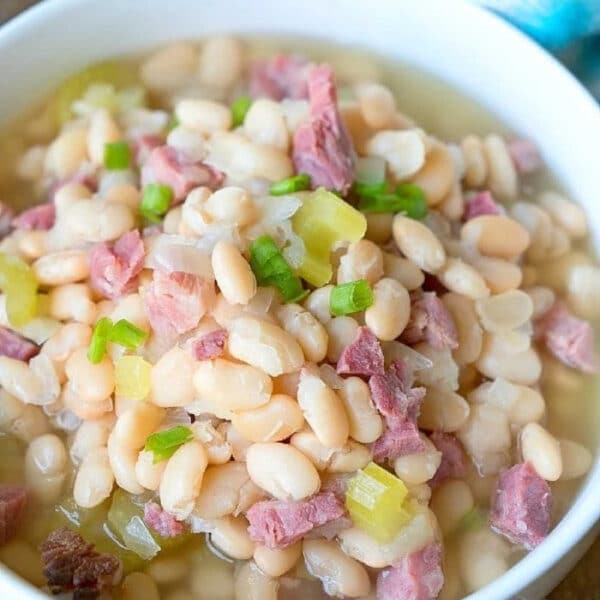 A bowl of pressure cooker ham and beans soup with pieces of ham and chopped green onions on top.
