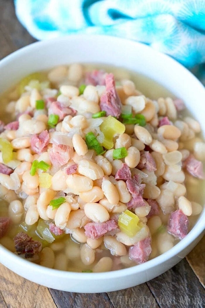 A bowl of pressure cooker ham and beans soup with pieces of ham and chopped green onions on top.