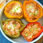 Four halved bell peppers filled with rice, cheese, and green onions, served in a white bowl—an inviting stuffed green peppers recipe perfect for any meal.