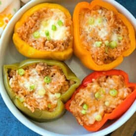 Four halved bell peppers filled with rice, cheese, and green onions, served in a white bowl—an inviting stuffed green peppers recipe perfect for any meal.