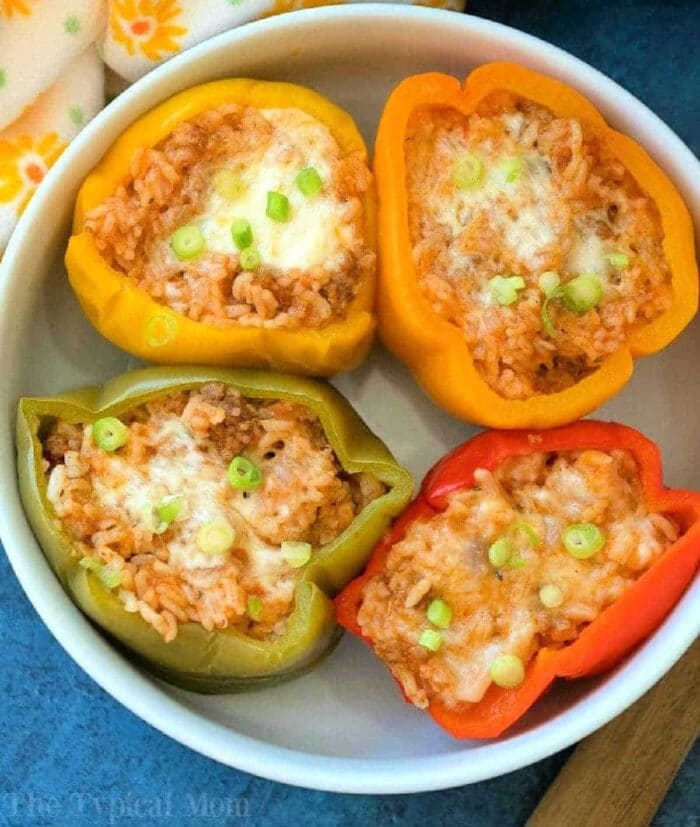 Four halved bell peppers filled with rice, cheese, and green onions, served in a white bowl—an inviting stuffed green peppers recipe perfect for any meal.
