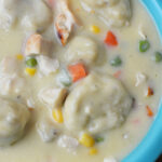 Creamy Chicken and Dumplings soup with vegetables in a blue bowl, made easy with Bisquick for fluffy dumplings—comfort food at its finest.