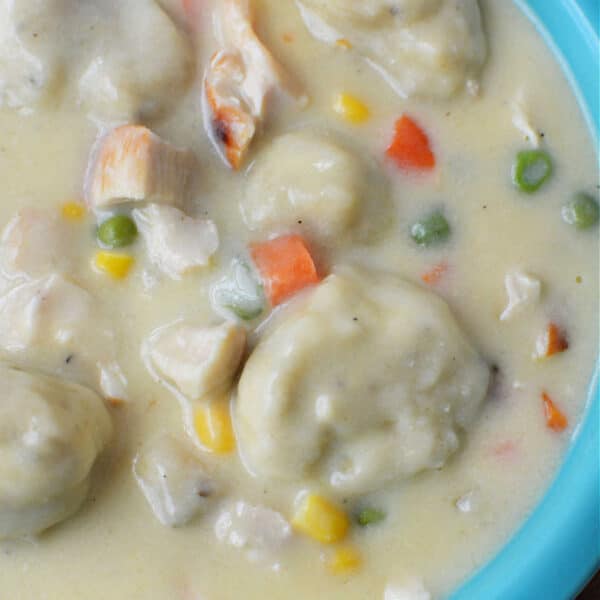 Creamy Chicken and Dumplings soup with vegetables in a blue bowl, made easy with Bisquick for fluffy dumplings—comfort food at its finest.