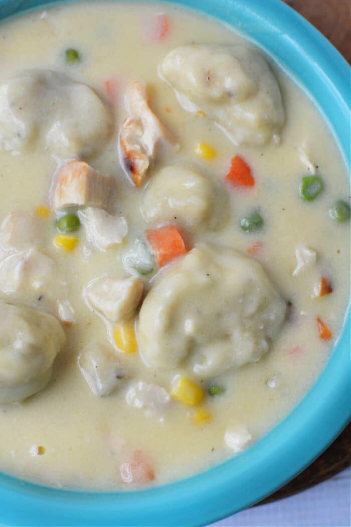 Creamy Chicken and Dumplings soup with vegetables in a blue bowl, made easy with Bisquick for fluffy dumplings—comfort food at its finest.