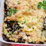 Baked vegetarian casserole topped with melted cheese, breadcrumbs, and parsley in a red baking dish—a delicious eggplant recipe perfect for any meal.