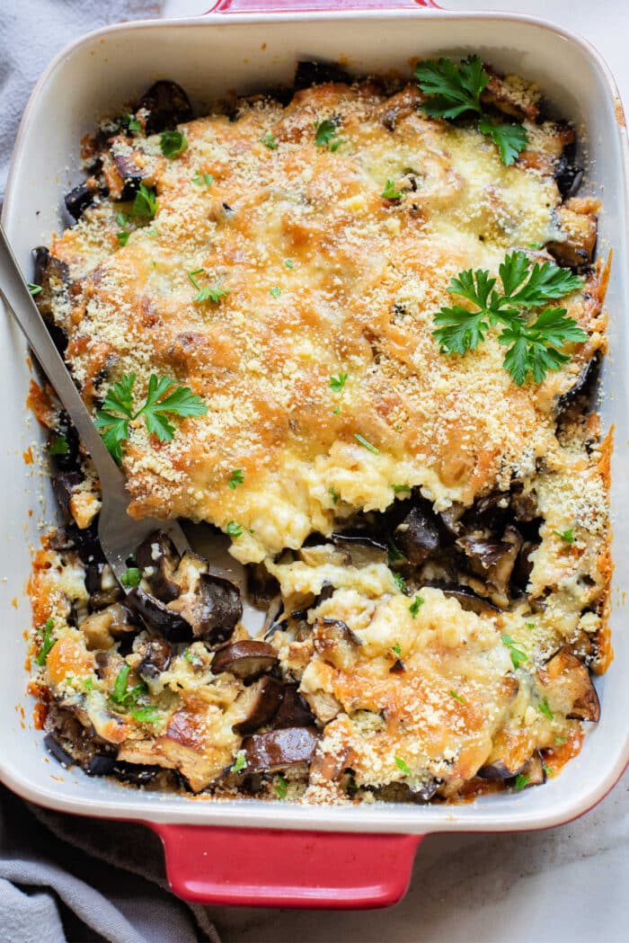 Eggplant Casserole baked to perfection, topped with melted cheese, golden breadcrumbs, and fresh parsley, served in a vibrant red baking dish.