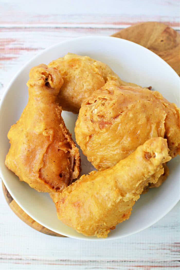 Four pieces of golden, crispy pan fried chicken on a white plate atop a wooden surface.