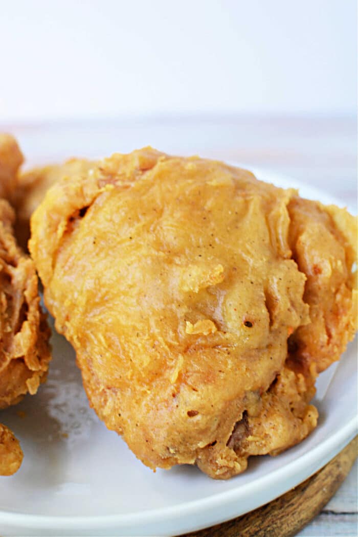 A piece of golden, crispy Pan Fried Chicken thighs sits on a white plate, ready to enjoy.