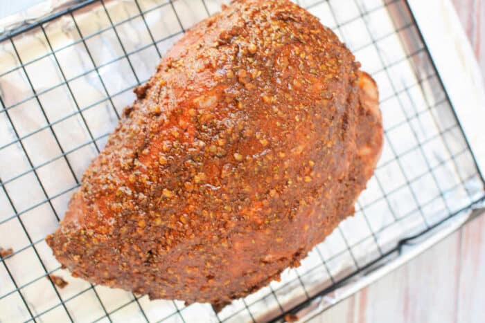 Seasoned ham on a wire rack over a foil-lined baking sheet, prepared just like a classic pork roast recipe, ready for the oven.