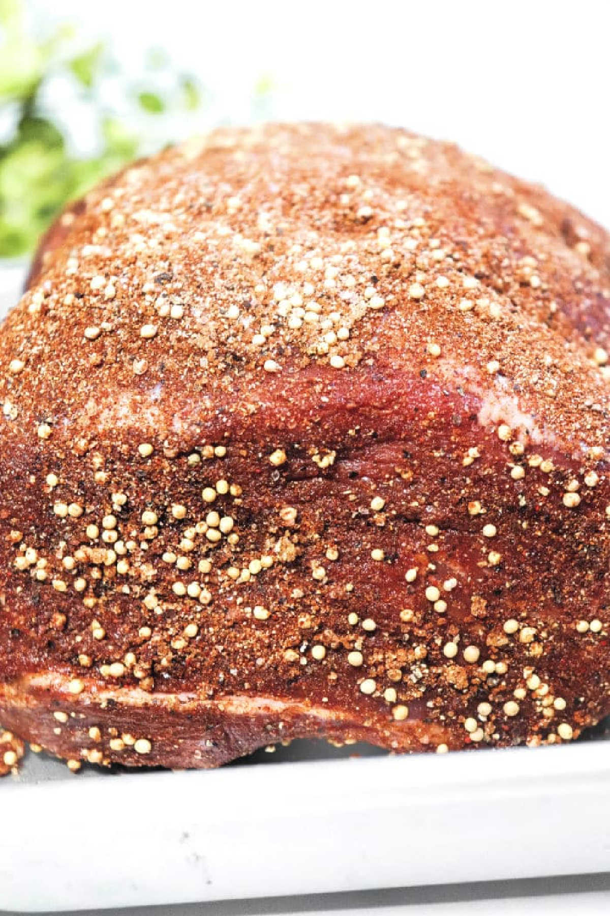 Smoked Sirloin Tip Roast coated in a spice rub and mustard seeds, resting on a white tray.