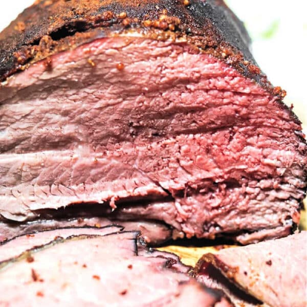 Sliced smoked beef brisket showing a pink, juicy interior and a seasoned, charred outer crust, similar to the rich flavor found in a Smoked Sirloin Tip Roast.