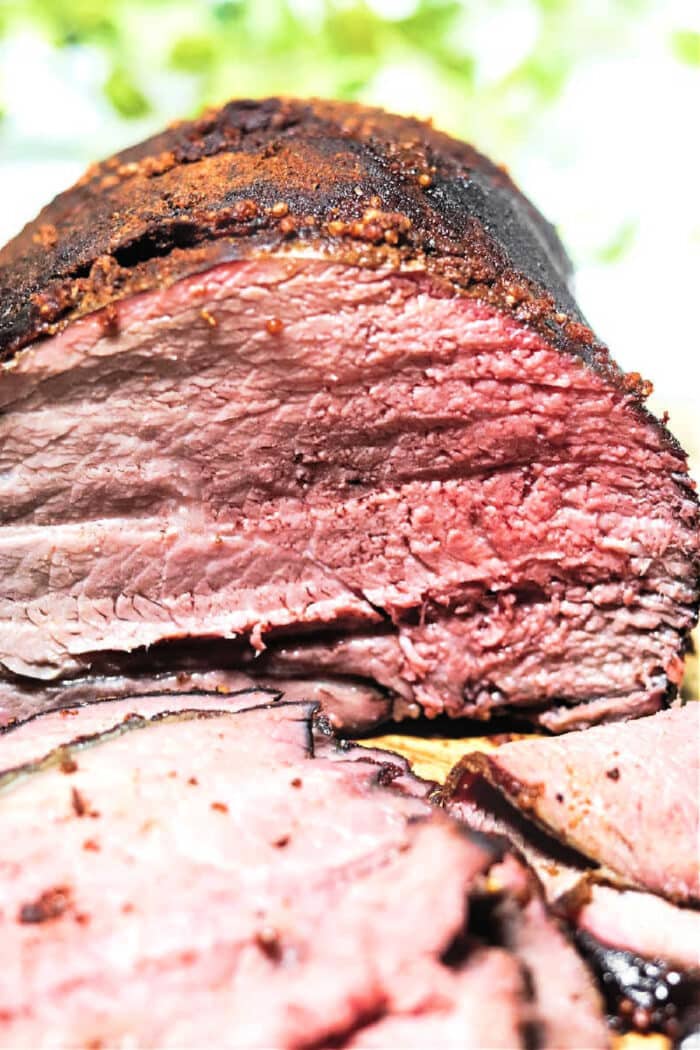 Sliced smoked beef brisket showing a pink, juicy interior and a seasoned, charred outer crust, similar to the rich flavor found in a Smoked Sirloin Tip Roast.