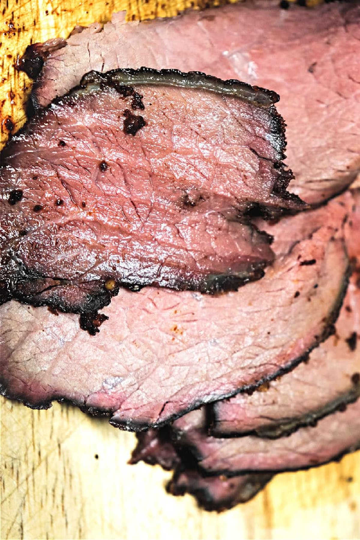 Sliced smoked sirloin tip roast with a dark crust on a wooden cutting board, served alongside tender Smoked Sirloin Tip Roast for a hearty meal.